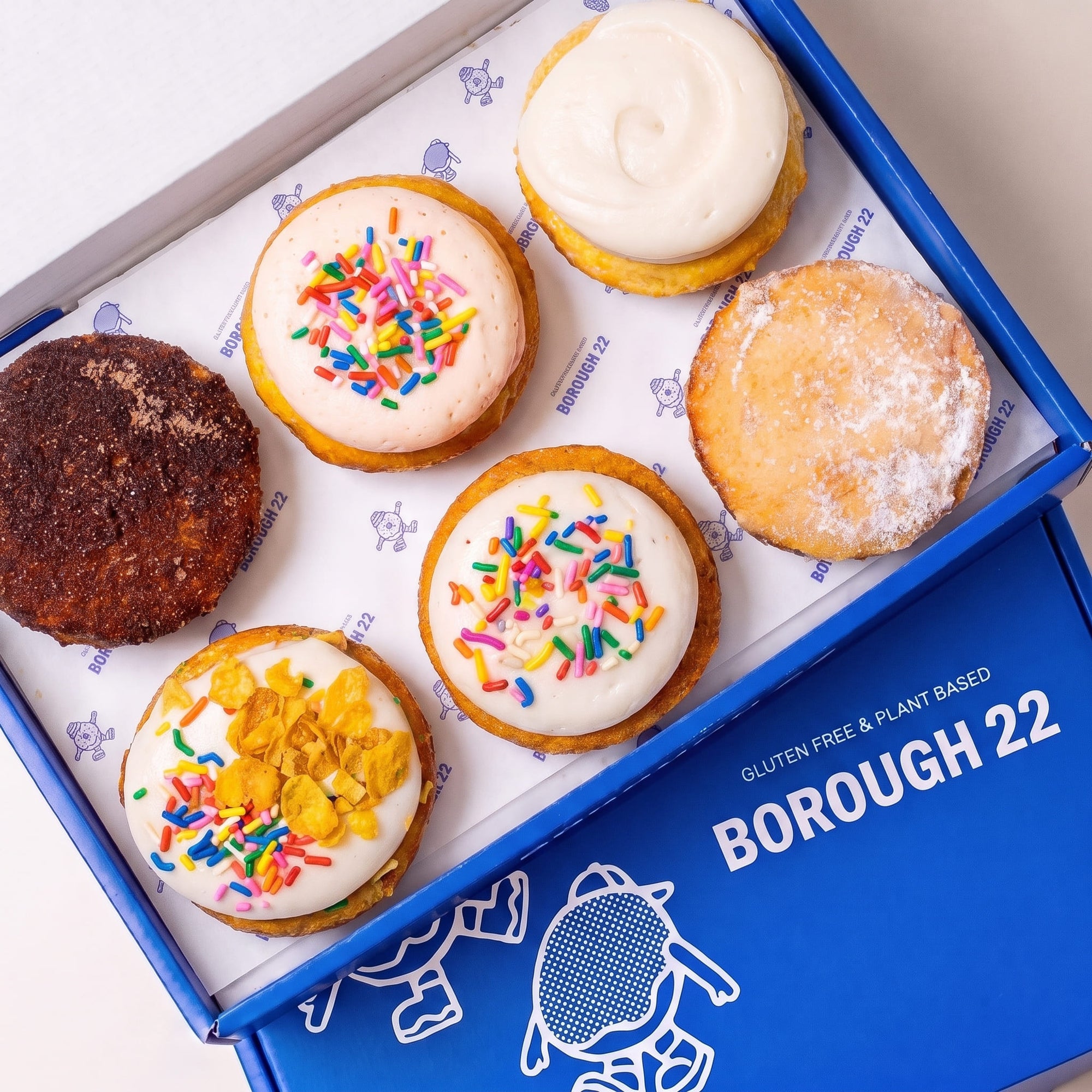 Open Borough 22 box of six gluten free vegan baked doughnuts, cinnamon sugar, vanilla glazed, pink and white iced with rainbow sprinkles, and cereal milk topped with cornflakes