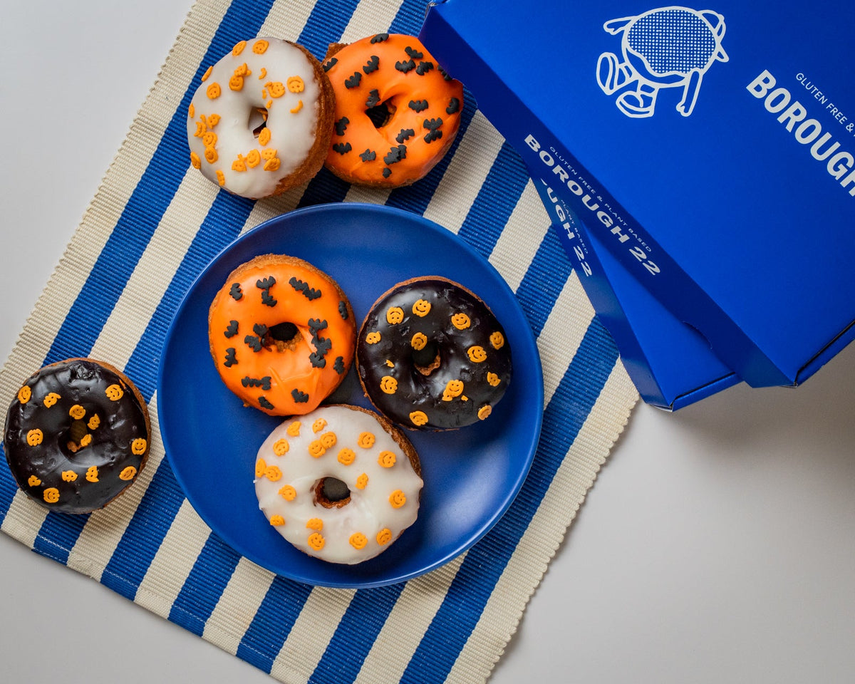 Gluten free vegan Halloween doughnuts with orange, black and white glazes and bat and pumpkin sprinkles beside a Borough 22 box