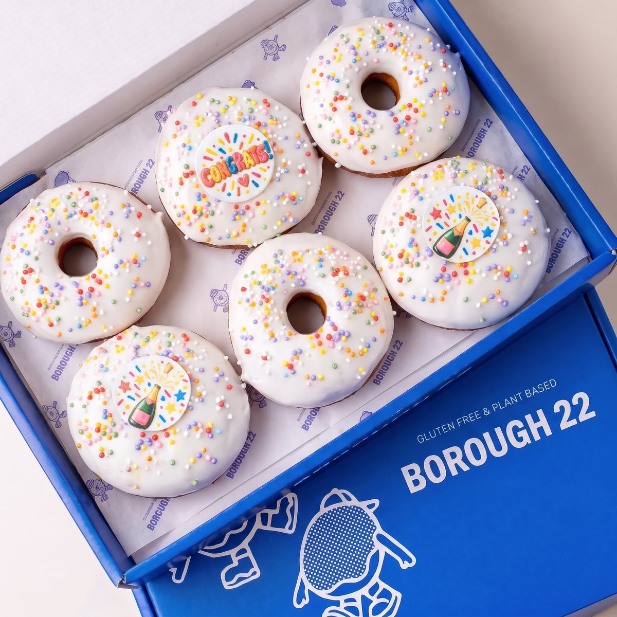 Gluten free vegan celebration doughnuts with white icing, rainbow sprinkles and Congrats and champagne toppers in a Borough 22 box