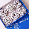 Gluten free vegan football doughnuts with white icing, black strand sprinkles and football toppers in a Borough 22 box