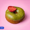 Gluten free vegan fried matcha doughnut with green glaze and a freeze dried strawberry