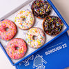Open Borough 22 box of six gluten free vegan fried ring doughnuts iced in pink, white and chocolate, all covered in rainbow sprinkles
