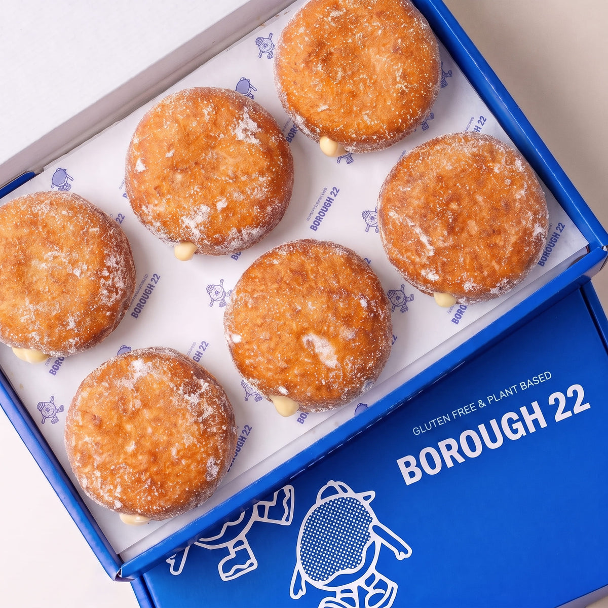 Open Borough 22 box of six gluten free vegan fried sugared doughnuts filled with vanilla custard, the filling visible at the side of each one