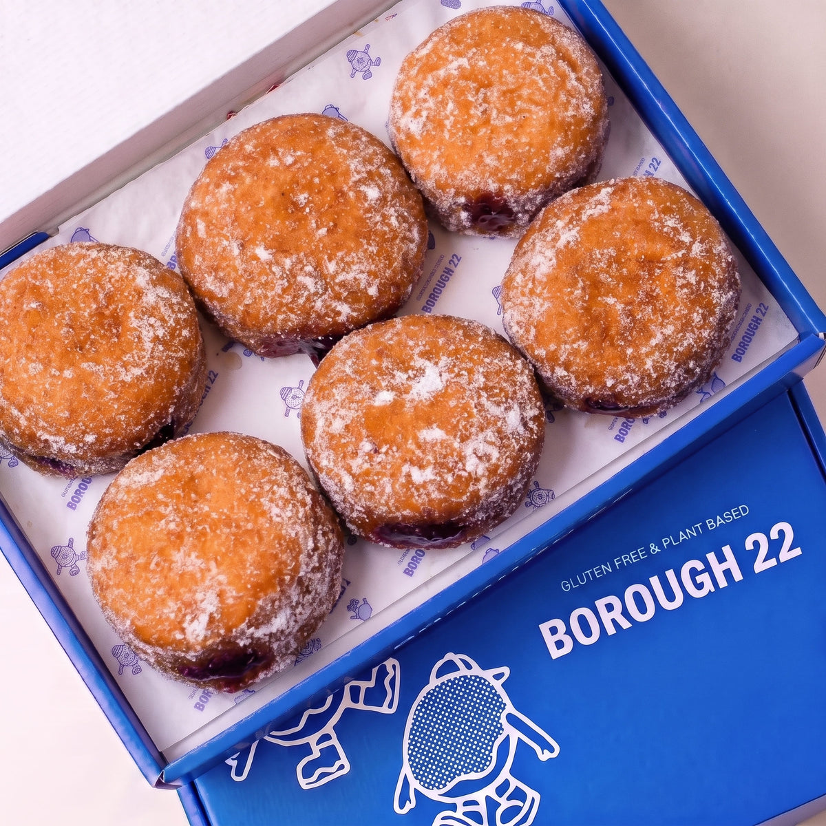 Open Borough 22 box of six gluten free vegan fried sugared doughnuts filled with raspberry jam, the filling visible at the side of each one