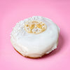 Gluten free vegan doughnut with white icing, pearl sprinkles and a gold champagne glasses topper