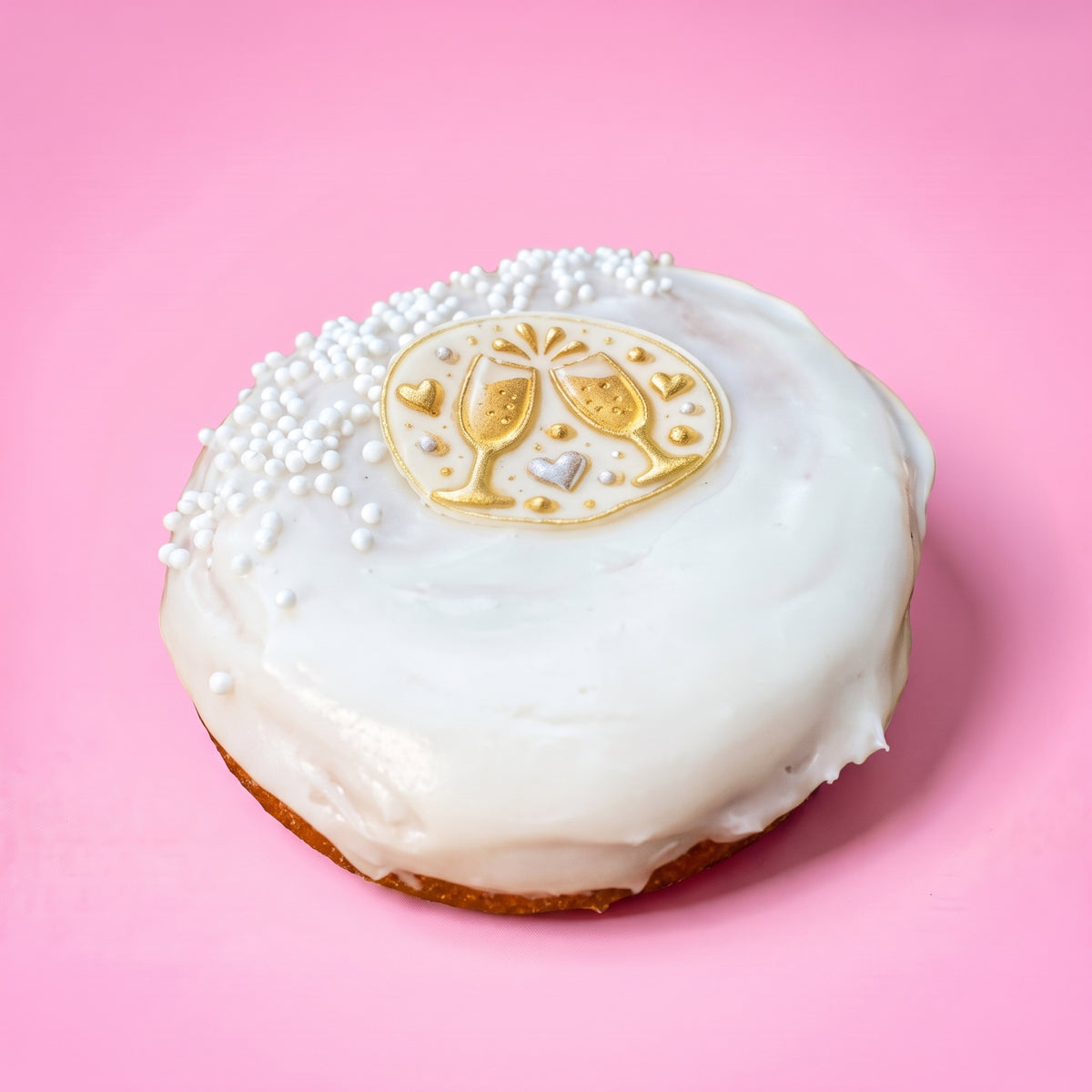 Gluten free vegan doughnut with white icing, pearl sprinkles and a gold champagne glasses topper