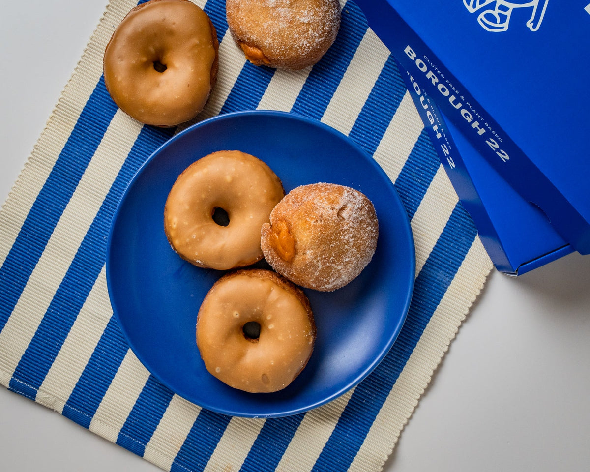 Gluten free vegan maple glazed ring doughnuts and sugared pumpkin custard doughnuts on a blue plate beside a Borough 22 box