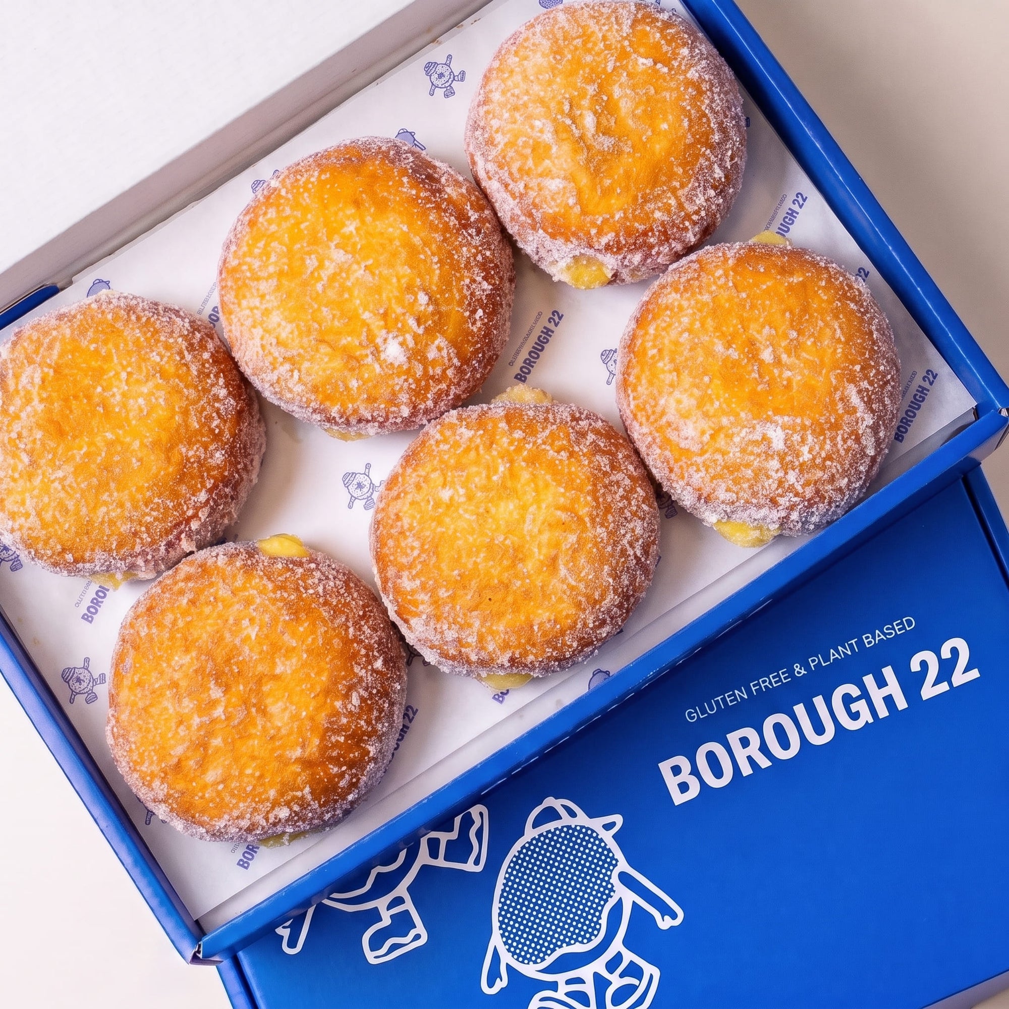 Open Borough 22 box of six gluten free oat free vegan fried sugared doughnuts filled with lemon curd, the filling visible at the side of each one