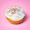 Gluten free vegan party doughnut with white icing, rainbow sprinkles and a Let's Celebrate topper