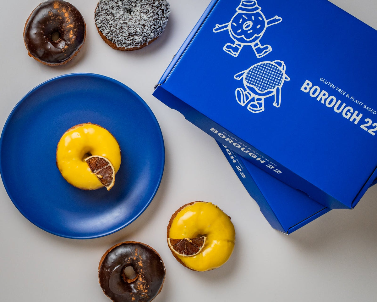 Gluten free vegan doughnuts with cocoa and mango glazes, finished with dried citrus, beside a Borough 22 box