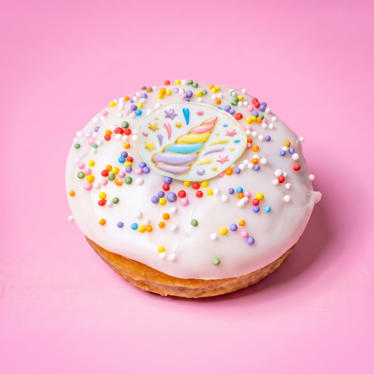 Gluten free vegan unicorn doughnut with white icing, pastel sprinkles and a rainbow unicorn horn topper