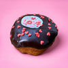 Gluten free vegan doughnut with chocolate icing, red heart sprinkles and a Love topper