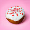 Gluten free vegan doughnut with white icing, red heart sprinkles and a Love topper