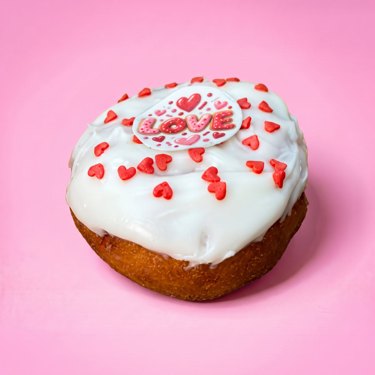 Gluten free vegan doughnut with white icing, red heart sprinkles and a Love topper